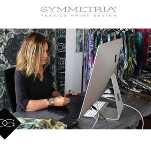 May include: A woman working on a digital tablet at a desk, with a large computer monitor in front of her. The image includes the text "SYMMETRIA TEXTILE PRINT DESIGN" and a logo. Colorful fabric designs hang in the background.