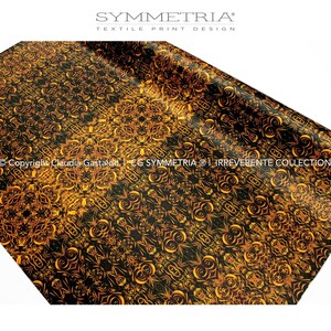 May include: A black and gold textile print with an intricate, symmetrical pattern. The design features swirling, floral-like motifs in shades of gold against a black background. The image includes the text "SYMMETRIA TEXTILE PRINT DESIGN".