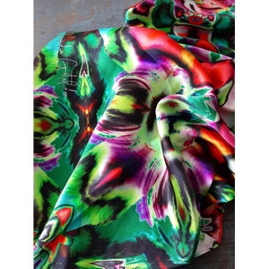 May include: A vibrant green, red, purple, and black silk scarf with a floral pattern. The scarf is folded and draped over a textured surface.