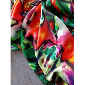 May include: Close-up of a colorful fabric with abstract patterns in shades of red, pink, green, and black. The fabric has a silky texture and a flowing drape.