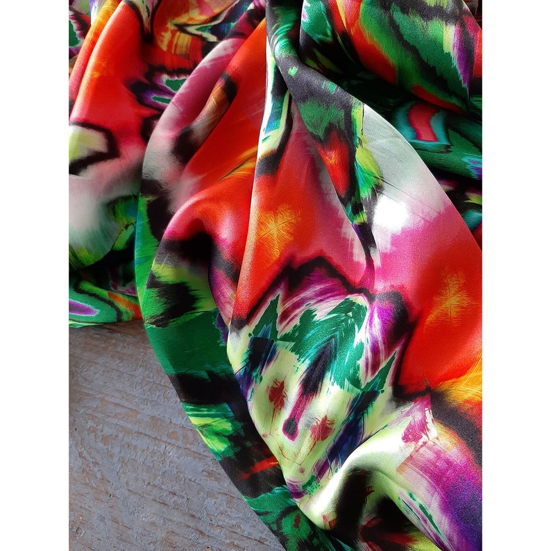 May include: Close-up of a colorful fabric with abstract patterns in shades of red, pink, green, and black. The fabric has a silky texture and a flowing drape.