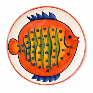 Op de afbeelding: Een rond keramieken bord met een crèmekleurige achtergrond en een handgeschilderd oranje visontwerp. De vis heeft groene verticale strepen, blauwe stippen en blauwe vinnen. Het bord heeft een dunne oranje rand langs de cirkelvormige rand.