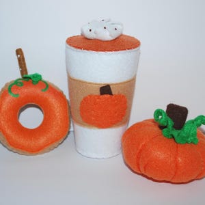May include: A felt pumpkin spice latte, donut, and pumpkin. The latte is white with an orange top and whipped cream. The donut is orange with a green stem. The pumpkin is orange with a green stem and brown top.