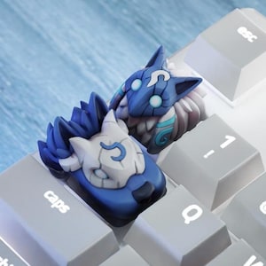 Könnte beinhalten: Zwei blaue und weiße wolfskopf-förmige Tastenkappen für eine Tastatur. Die Tastenkappen sind mit einem Wolfskopf gestaltet und haben ein blaues und weißes Farbschema.
