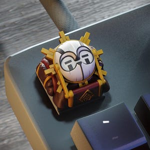 Può includere: Un keycap artigianale personalizzato con un design stilizzato del viso. Il keycap ha un viso bianco con accenti neri e viola, circondato da raggi di sole dorati. La base è marrone con dettagli dorati e rossi.