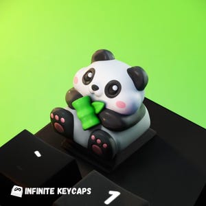 Puede incluir: Un tapón de tecla de panda blanco y negro sosteniendo un brote de bambú verde. El tapón de tecla está sentado en un teclado negro.
