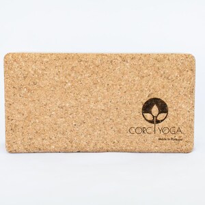 Puede incluir: Un bloque de yoga rectangular de corcho con un logotipo marrón que dice "CORK YOGA" y "Made in Portugal".