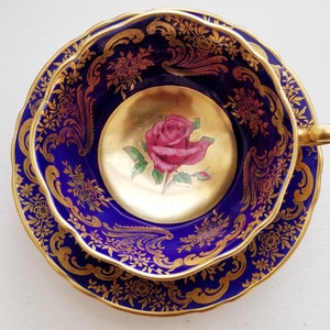Può includere: Servizio da tè blu cobalto con dettagli dorati. La tazza ha un interno dorato con una rosa rosa dipinta. Il set ha un bordo smerlato ed è probabilmente vintage. Misure in centimetri.