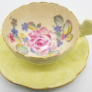 May include: A yellow teacup and saucer set with a floral design. The cup has a butterfly handle and the saucer has a scalloped edge.