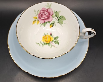 May include: A vintage teacup and saucer set with a delicate floral design. The cup features a pink rose with yellow accents and green leaves, while the saucer is a light blue color with a gold trim.
