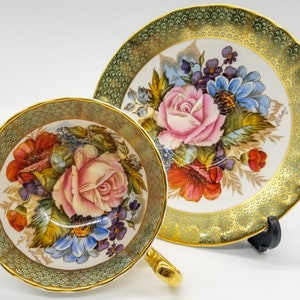 Peut inclure: Une tasse à thé et une soucoupe vintage avec un motif floral vert et or. La tasse et la soucoupe présentent un délicat motif floral avec des fleurs roses, rouges, bleues et jaunes. La soucoupe a un bord festonné et une bordure dorée.
