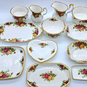 Puede incluir: Colección de vajilla de porcelana blanca con un diseño floral de rosas en tonos rojos, amarillos y rosas, con bordes dorados. Incluye fuentes, cuencos y jarras de crema.