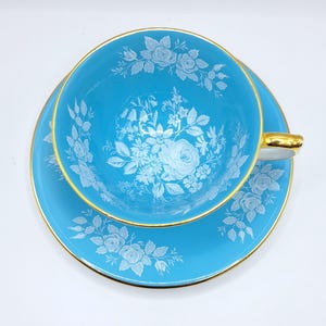 May include: A vintage turquoise teacup and saucer set. The cup and saucer feature a white floral design and gold trim. The teacup has a handle with a gold accent. The set is designed for tea parties and special occasions.
