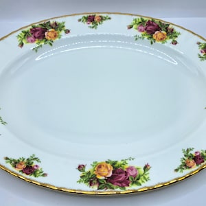 Puede incluir: Plato ovalado blanco con borde dorado y estampado floral de rosas. Las rosas son en tonos de rojo, amarillo y rosa con hojas verdes. Una pieza decorativa para servir alimentos.
