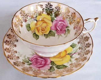 May include: A vintage teacup and saucer set with a pink and white base and gold trim. The set features a floral design with yellow and pink roses.