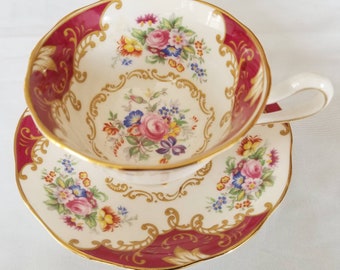 May include: A vintage teacup and saucer set with a floral pattern and gold trim. The cup and saucer are white with a burgundy rim and gold accents. The floral pattern features pink, yellow, and blue flowers.