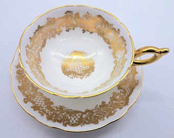 May include: A white teacup and saucer with a gold, intricate floral pattern. The cup has a gold handle.