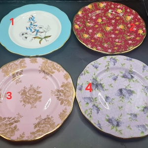 May include: Four decorative plates with scalloped edges. One plate is light blue with a floral design, another is red with a floral pattern, a third is pink with gold roses, and the last is lavender with a floral pattern.
