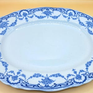 May include: Oval serving platter with a white center and a blue floral and scrollwork border. The rim has a scalloped edge. The blue design includes floral bouquets and decorative urns. The platter is likely made of ceramic.