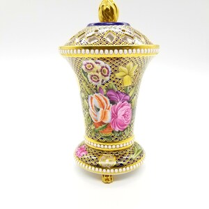 May include: A gold and blue porcelain vase with a floral design and a pierced lid. The vase has a scalloped rim and a beaded trim.