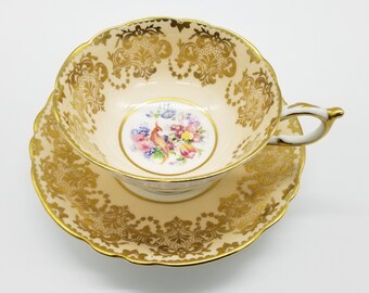 May include: A delicate teacup and saucer set with a floral design and a gold trim. The cup features a bird and floral motif in the center.