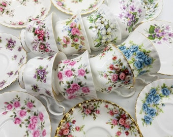 May include: A collection of vintage teacups and saucers with floral patterns in shades of pink, blue, purple, and white.
