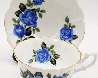 May include: A white teacup and saucer set with a blue rose pattern. The cup and saucer have a gold trim.