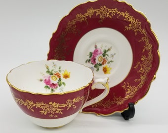 May include: A red and white teacup and saucer set with a gold floral design. The cup and saucer have a scalloped edge.