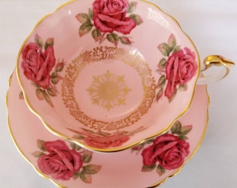 May include: A pink teacup and saucer set with a gold trim and a floral design featuring pink roses.