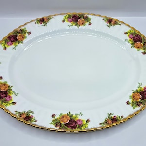 Puede incluir: Plato ovalado para servir con centro blanco y borde dorado festoneado. El borde está decorado con racimos de rosas en tonos rojos, naranjas y rosas, con hojas verdes. Una pieza clásica para servir alimentos.