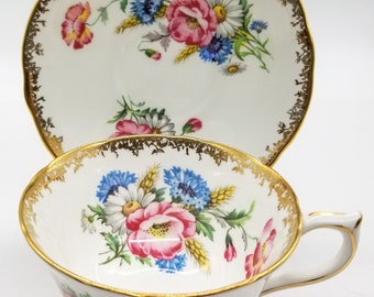May include: A white teacup and saucer with a gold rim and floral pattern. The flowers are pink, blue, and yellow.