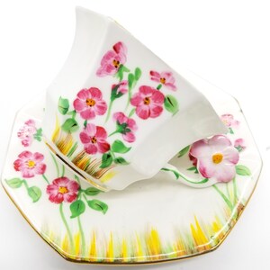 May include: A white porcelain teacup and saucer set with a floral design. The cup and saucer are decorated with pink flowers and green leaves on a white background. The saucer has a gold rim.