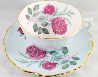 May include: A delicate teacup and saucer set with a light blue background and a floral design featuring pink roses and green leaves. The edges of the cup and saucer are trimmed with gold.