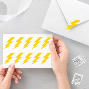 Könnte beinhalten: Ein Blatt weißes Papier mit 12 gelben Blitz-Aufklebern. Die Aufkleber sind in zwei Reihen zu sechs angeordnet.