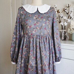 May include: A blue floral dress with a white peter pan collar and long sleeves. The dress has a gathered skirt and a fitted bodice.