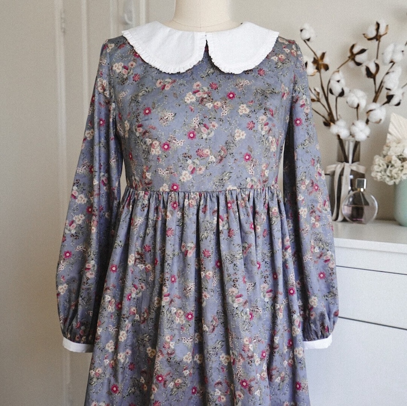 May include: A blue floral dress with a white peter pan collar and long sleeves. The dress has a gathered skirt and a fitted bodice.