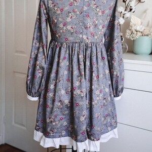May include: A blue and white floral dress with long sleeves and a white ruffle trim. The dress has a gathered waist and a full skirt.