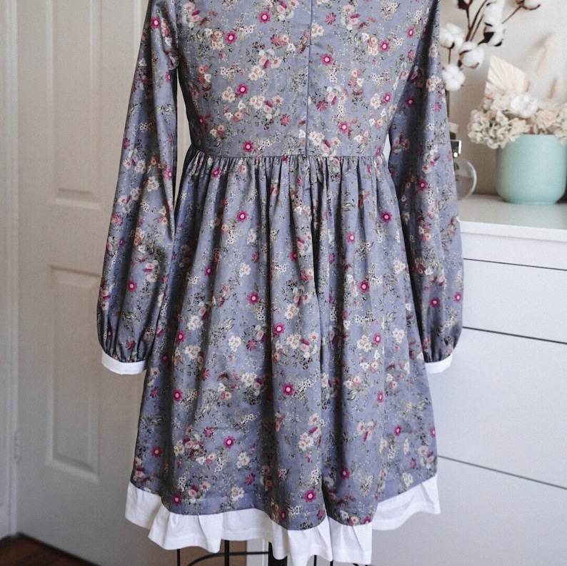 May include: A blue and white floral dress with long sleeves and a white ruffle trim. The dress has a gathered waist and a full skirt.