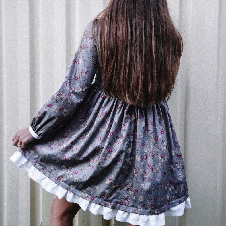 May include: A gray floral dress with a white ruffle trim. The dress has long sleeves and a gathered skirt.