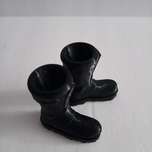 May include: Two miniature black rubber boots. The boots have a glossy finish and are set against a white background. The boots are a small size, and the details of the boot are visible, including the sole and the top opening.