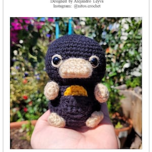 Puede incluir: Un Niffler de ganchillo hecho a mano de la serie Animales Fantásticos. El peluche es azul oscuro con un hocico beige, extremidades beige y una bolsa amarilla. La imagen incluye el texto "Fantastic Beasts Niffler Crochet Pattern".