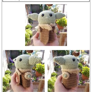 May include: A green crocheted baby Yoda doll wearing a brown crocheted coat. The doll is being held in a hand with a green leafy background.