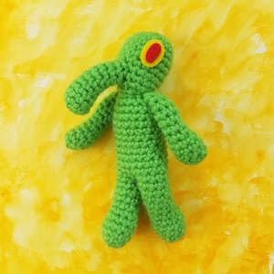 May include: Green crocheted plush toy shaped like a cartoon character with a red eye.