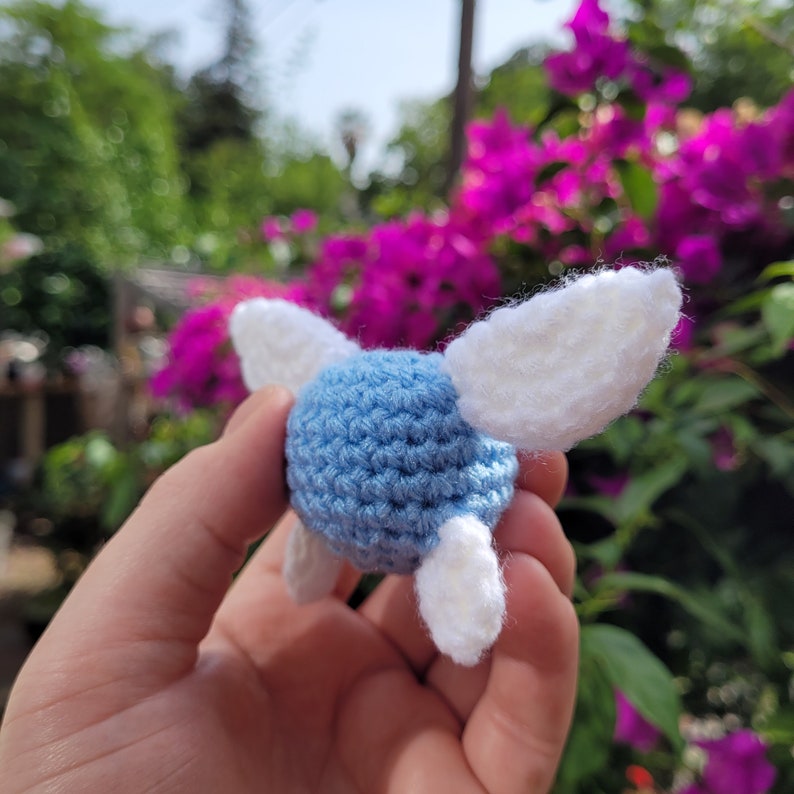 May include: A crocheted blue and white fairy with wings. The fairy is held in a hand.