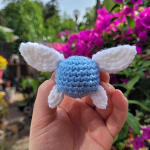 May include: A crocheted blue and white figurine of a fairy with wings. The fairy is holding its wings out to the sides.