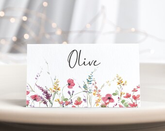 May include: A white place card with a watercolor floral design in shades of pink, yellow, and green. The name "Olive" is written in black cursive script.