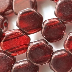 May include: A close-up of a strand of red glass beads. The beads are hexagonal in shape and have a slightly iridescent finish.