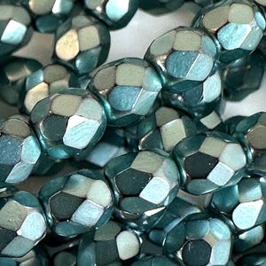 May include: Close-up of strands of teal-colored faceted beads. The beads have a metallic sheen and a multi-faceted design, reflecting light. The beads are strung together, suggesting they are for jewelry making or crafting.