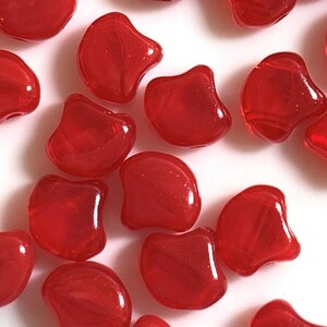 May include: A collection of red glass beads in a teardrop shape with a slight curve. The beads have a glossy finish.