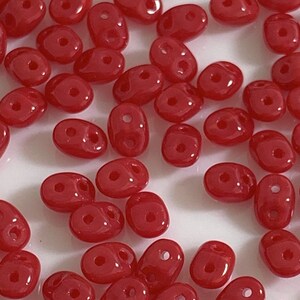 May include: A large quantity of small, red, oval-shaped glass beads with two holes in each bead.